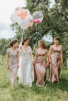 le demoiselles d'honneur Regardez à le souriant la mariée. le la mariée et sa amusement copains célébrer une bachelorette fête en plein air dans correspondant à Robes. le la mariée et copains sur le herbe en dessous de le ouvert ciel photo