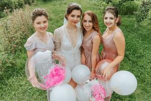 le demoiselles d'honneur Regardez à le souriant la mariée. le la mariée et sa amusement copains célébrer une bachelorette fête en plein air dans correspondant à Robes. le la mariée et copains sur le herbe en dessous de le ouvert ciel photo