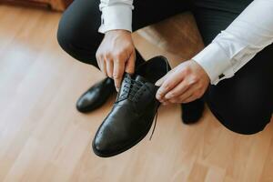 une élégant jeune marié est en train de préparer pour le mariage cérémonie. du marié Matin. le homme d'affaire porte noir chaussures. le jeune marié est avoir prêt dans le Matin avant le mariage la cérémonie photo