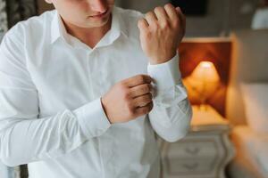 une élégant jeune marié est en train de préparer pour le mariage cérémonie. du marié Matin. homme d'affaire dans blanc chemise dans hôtel, Masculin mains fermer, jeune marié avoir prêt dans Matin avant mariage la cérémonie photo