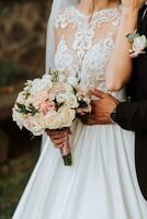 mignonne brunette la mariée dans blanc robe et bouquet de fleurs étreindre en plein air. mariage la photographie, portrait de souriant jeunes mariés. photo