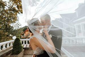 magnifique content luxueux brunette la mariée et élégant élégant jeune marié permanent en dessous de une voile photo