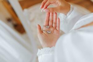 le la mariée détient dans sa mains et spectacles sa des boucles d'oreilles avec précieux des pierres, fermer. Matin de le la mariée. le mariage journée. photo