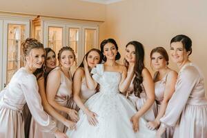 élégant magnifique demoiselles d'honneur dans correspondant à soie Robes portion magnifique brunette la mariée dans blanc robe avoir prêt pour mariage, Matin les préparatifs, femme en mettant sur robe photo