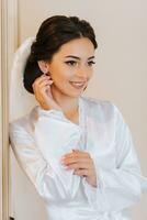 content brunette la mariée dans blanc peignoir avec longue voile professionnel maquillage et coiffure dans chambre à coucher. photo