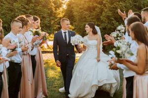 large angle coup de la mariée et jeune marié en marchant vers le bas le rayon après leur mariage la cérémonie à le coucher du soleil comme copains et famille célébrer photo