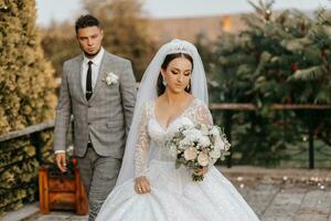 Jeune mariage couple profiter romantique des moments en plein air sur une été prairie. une la mariée avec une couronne sur sa tête et une longue voile. jeune marié dans une classique gris costume photo