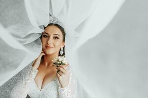 femelle beauté. mignonne femme à maison. le la mariée pose pour le photographe. une élégant femme porte une blanc robe. professionnel maquillage et cheveux. le la mariée a une couronne sur sa tête et une longue voile. photo