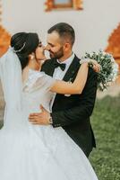 portrait de le la mariée et jeune marié embrasser contre le Contexte de le l'automne Soleil de vert des arbres dans le jardin ou parc. un incroyablement magnifique la mariée. élégant jeune marié avec une barbe photo