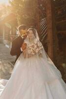 magnifique la mariée en dessous de une voile dans une à la mode mariage robe sur une Naturel Contexte dans le parc à le coucher du soleil. une étourdissant Jeune la mariée est incroyablement heureux. content fille sur sa mariage journée photo