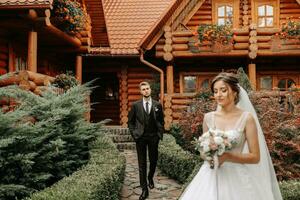 magnifique élégant luxe la mariée avec voile et élégant jeune marié en marchant sur le rue près grand l'automne des arbres et en bois Maisons photo