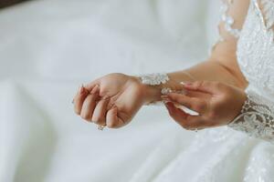 les filles mains fermer, le la mariée est en train de préparer pour le mariage. le la mariée attache le dentelle manches. magnifique mains. Matin de le la mariée. détails à le mariage photo