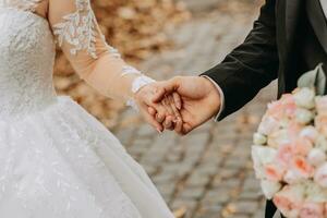 une élégant jeune marié dans une noir costume et une mignonne la mariée dans une blanc robe avec une longue voile sont en marchant dans le parc. fermer mariage portrait de le mains de le content jeunes mariés. photo