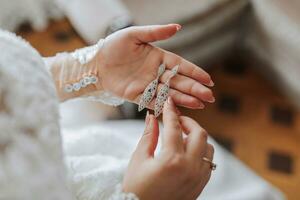 le la mariée détient dans sa mains et spectacles sa des boucles d'oreilles avec précieux des pierres, fermer. Matin de le la mariée. le mariage journée. photo