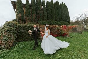 le la mariée et jeune marié sont en marchant dans le l'automne parc près le loger, mariage cérémonie, côté voir. le la mariée et jeune marié contre le Contexte de jauni l'automne feuilles et grand des arbres. photo