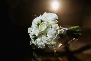 accessoires sur le du marié mariage journée. une bouquet de blanc des roses sur une foncé Contexte avec rétro-éclairage. Pour des hommes mode photo