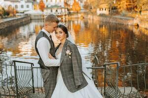 une fabuleux romantique nouveau marié couple est étreindre à le coucher du soleil dans un l'automne parc avec feuilles de des arbres sur le herbe photo