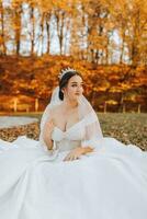 une magnifique la mariée est séance sur le herbe près le l'automne feuilles de le des arbres. mariage portrait de une Jeune la mariée dans un l'automne thème. mariage la photographie. photo