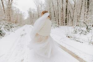 une magnifique la mariée dans blanc est en marchant vers le bas le route dans une fabuleux neigeux hiver forêt. portrait de le la mariée dans la nature. magnifique la mariée dans une blanc robe dans une hiver forêt. photo