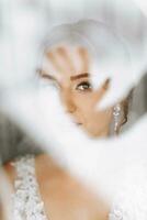 une magnifique et doux la mariée regards en dehors le fenêtre dans le Matin. photo par le la fenêtre. magnifique Naturel se maquiller. mariage coiffure. Matin de le la mariée.