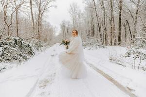 une magnifique la mariée dans une blanc robe avec une bouquet de fleurs dans une fabuleux neigeux hiver forêt. portrait de le la mariée dans la nature. magnifique la mariée dans une blanc robe dans une hiver forêt. photo