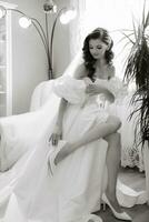 magnifique modèle fille avec longue frisé cheveux dans une à la mode mariage robe. verticale portrait. une magnifique la mariée dans une blanc mariage robe porte talon haut chaussures. noir et blanc photo