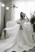 magnifique modèle fille avec longue frisé cheveux dans une à la mode mariage robe. verticale portrait. une magnifique la mariée dans une blanc mariage robe détient des chaussures dans sa mains. noir et blanc photo