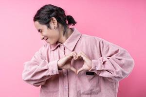 jeune homme asiatique aux cheveux longs, vêtu d'une chemise rose, souriant sur fond rose photo