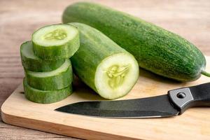 aliments végétaux au concombre coupés en tranches et couteau sur une planche à découper pour la cuisson dans la cuisine. photo
