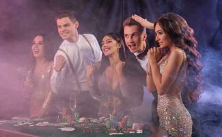 copains en jouant poker à casino, à table avec piles de puces, argent, cartes, Champagne sur il. célébrer gagner, excité. noir Contexte. fermer. photo