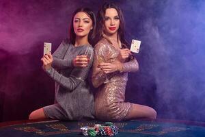 deux les filles sont en jouant poker à casino, en portant des lunettes de Champagne et cartes, séance sur table avec frites sur il. noir, fumée Contexte. fermer. photo