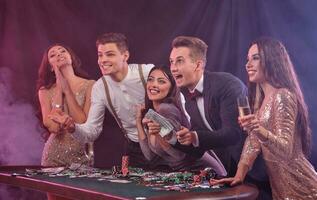 copains en jouant poker à casino, à table avec piles de puces, argent, cartes, Champagne sur il. célébrer gagner, excité. noir Contexte. fermer. photo