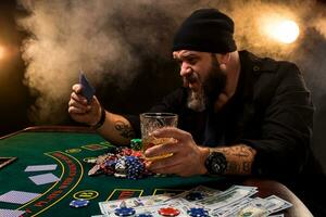 barbu homme avec cigare et verre séance à poker table dans une casino. jeu, en jouant cartes et roulette. photo