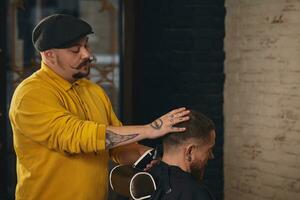 Barbier faisant la coupe de cheveux d'un homme barbu attrayant en salon de coiffure photo