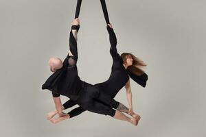 magnifique fille et un athlétique homme dans une noir sport costume sont performant un acrobatique éléments dans une studio. photo