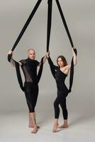 magnifique fille et un athlétique homme dans une noir sport costume sont performant un acrobatique éléments dans une studio. photo