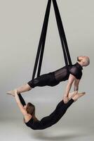 magnifique fille et un athlétique homme dans une noir sport costume sont performant un acrobatique éléments dans une studio. photo