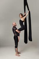 magnifique fille et un athlétique homme dans une noir sport costume sont performant un acrobatique éléments dans une studio. photo