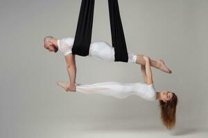 magnifique fille et un athlétique homme dans une blanc sport costume sont performant un acrobatique éléments dans une studio. photo