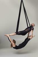 magnifique fille et un athlétique homme dans une noir sport costume sont performant un acrobatique éléments dans une studio. photo