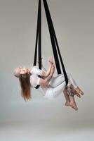 magnifique fille et un athlétique homme dans une blanc sport costume sont performant un acrobatique éléments dans une studio. photo