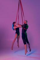 magnifique fille et un athlétique homme dans une noir sport costume sont performant un acrobatique éléments dans une studio. photo