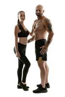 athlétique homme dans noir short et baskets avec brunette femme dans leggings et Haut posant isolé sur blanc Contexte. aptitude couple, Gym concept. photo