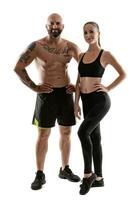 athlétique homme dans noir short et baskets avec brunette femme dans leggings et Haut posant isolé sur blanc Contexte. aptitude couple, Gym concept. photo