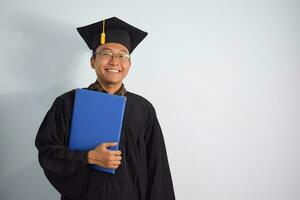 expressif de adulte Indonésie Masculin porter l'obtention du diplôme peignoir, chapeau et lunettes, asiatique Masculin l'obtention du diplôme apporter Vide bleu certificat isolé sur blanc arrière-plan, expressions de portrait l'obtention du diplôme photo