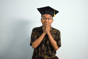 expressif de adulte Indonésie Masculin porter batique, toge tasse ou l'obtention du diplôme chapeau et lunettes isolé sur blanc arrière-plan, expressions de portrait l'obtention du diplôme photo