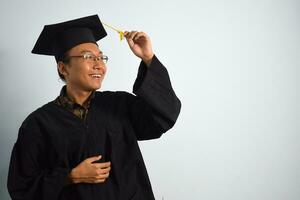 expressif de adulte Indonésie Masculin porter l'obtention du diplôme peignoir, chapeau et lunettes isolé sur blanc arrière-plan, expressions de portrait l'obtention du diplôme photo