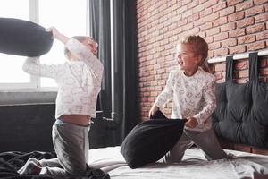 vilains enfants petit garçon et fille ont organisé une bataille d'oreillers sur le lit dans la chambre. ils aiment ce genre de jeu photo