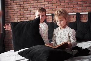 vilains enfants petit garçon et fille ont organisé une bataille d'oreillers sur le lit dans la chambre. ils aiment ce genre de jeu photo