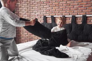 vilains enfants petit garçon et fille ont organisé une bataille d'oreillers sur le lit dans la chambre. ils aiment ce genre de jeu